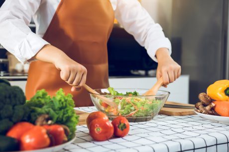 Asian woman is mixing the ingredients in a salad bowl at the kitchen cooking table.